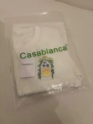Vit t-shirt från Casablanca S - Vit t-shirt från Casablanca med tryckt logga och färgglad illustration på bröstet. Klassisk rund hals och korta ärmar. Tillverkad i mjuk bomull för en skön känsla. Perfekt för en clean och stilren look.
