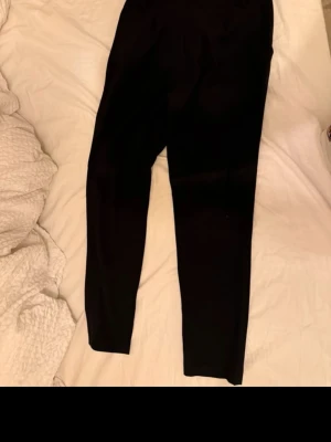 Svarta kostymbyxor med hög midja - Säljer ett par klassiska svarta kostymbyxo. De är stretchiga och mjuka, perfekta till oversized tröjor eller hoodies. Materialet ser ut att vara bomull eller en bomullsblandning. Inga synliga detaljer eller loggor.