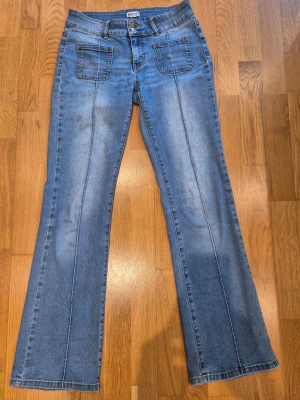 Blå bootcut jeans med fickor fram från MADLADY - Snygga blå bootcut jeans med markerade sömmar och fickor fram. Jeansen har även bakfickor med lock och knappdetalj. Klassisk ljus tvätt och lätt utsvängda ben ger en retrovibe.