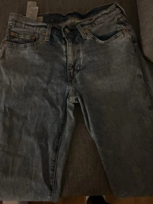Levi's ljusblå raka jeans - Säljer ett par klassiska ljusblå jeans från Levi's med rak passform och fem fickor. Jeansen har en vintage tvätt och tydliga sömmar, perfekt för en avslappnad och tidlös stil. Passar dig som gillar retrovibbar och denim med karaktär.