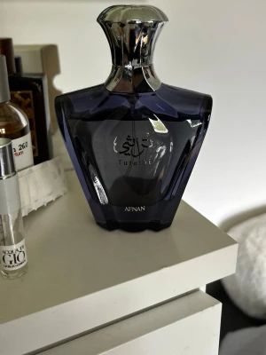 Afnan Tuflati parfymflaska - Snygg parfymflaska från Afnan, modellen Tuflati. Flaskan är mörkblå med silverfärgat lock och har en elegant, kantig form. Text i både arabiska och engelska på framsidan. Perfekt för dig som gillar exklusiva dofter och stilren design.