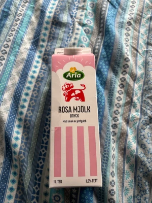 Arla Rosa Mjölk jordgubb 1L - En 1 liters förpackning Arla Rosa Mjölk med smak av jordgubb. Kartongen är vit med rosa ränder och har en röd ko på framsidan. Drycken innehåller 1,0% fett och är en smaksatt mjölkdryck.