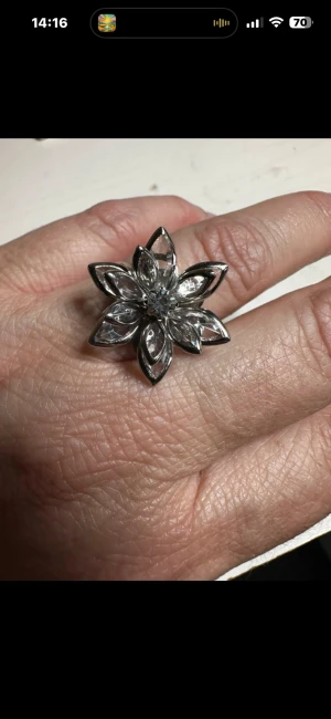 Blommig silverfärgad ring med stenar - Snygg ring i silverfärg med en stor blomformad design. Ringen har sex kronblad med glittrande klara stenar som ger en riktigt iögonfallande look. Perfekt för dig som gillar statement-smycken och vill sticka ut lite extra.