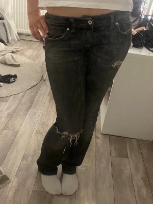 Svarta slitna jeans med hål - Säljer ett par svarta jeans med slitningar och hål vid knäna. Jeansen har klassisk femficksmodell, låg midja och raka ben. Perfekta för dig som gillar en edgy och avslappnad stil. 