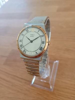 1980s Timex Q "Genta-style" Two-Tone 34mm - Säljer en otroligt vacker vintage dressklocka till herr från tidigt 80-tal (78-84) från välrenommerade Timex. Klockan är i mycket gott skick med tanke på ålder enligt bilder. Små tecken på användning och repor finns men inget som stör. Urverket går att ställa, justerbart originalarmband i två-tonat rostfritt stål, datumvisare, mineralglas, vattentät osv. Behöver nog bara nytt batteri, otestad.  Begagnat värde: 900+ SEK Mitt pris: 689 SEK  Skriv vid frågor och se gärna mina andra annonser! Skapar