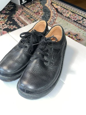 Svarta loafers från Clarks i läder - Säljer ett par svarta loafers från Clarks i äkta läder med snörning och rund tå. Skorna har en klassisk och tidlös design med diskret logga på sidan. Perfekta för dig som gillar stilrena och bekväma skor.
