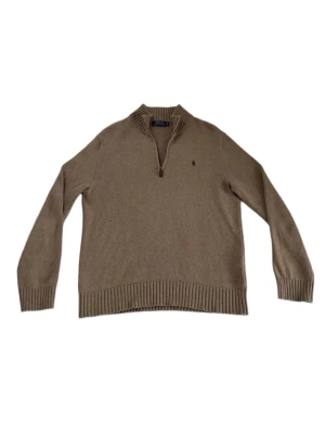 Polo Ralph Lauren Half Zip Sweater - Klassisk beige stickad tröja från Polo Ralph Lauren med halv dragkedja och ribbad krage. Tröjan har långa ärmar, ribbade muddar och den ikoniska broderade loggan på bröstet. Perfekt för lager på lager och stilren look.