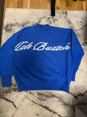 Blå stickad tröja Cole Buxton - Helt ny aldrig använd Snygg blå stickad tröja från Cole Buxton med vit logotyp i stor text över bröstet. Tröjan har rund halsringning, långa ärmar och ribbade muddar vid ärmslut och nederkant. Perfekt för dig som gillar streetwear och vill sticka ut.