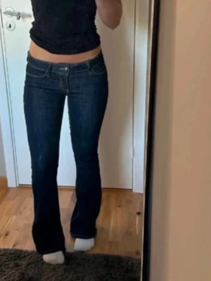 Mörkblå bootcut jeans med låg midja - Snygga mörkblå bootcut jeans med låg midja och klassiska fickor både fram och bak. Jeansen har kontrastsömmar och en figurnära passform upptill som släpper ut vid bensluten. Perfekta för en trendig och avslappnad look.