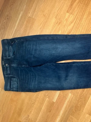 Mörkblå Replay Hyperflex jeans - Snygga mörkblå jeans från Replay med Hyperflex-teknologi som ger extra stretch och komfort. Klassisk femficksmodell med Replay-logga på bakfickan och grå patch i midjan. Perfekta för dig som vill ha både stil och rörelsefrihet. Helt oanvända säljer för det var fel storlek 