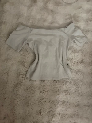 Vit offshoulder topp - Säljer en stilren vit offshoulder topp med korta ärmar. Toppen har en figurnära passform och är perfekt för dig som gillar en enkel men trendig look. Materialet känns mjukt och stretchigt, troligen bomull eller en bomullsblandning.