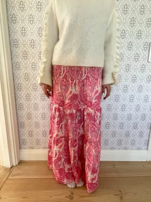 Rosa paisleymönstrad långkjol - Säljer en rosa långkjol med paisleymönster i vitt och rött. Kjolen har smock/resår i midjan. Står ej storlek eller märke i kjolen💝