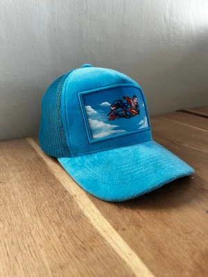 Blå Superman keps från TED wonti  - Cool blå keps från Ted wonti med mesh på sidorna och ett stort Superman-märke framtill. Kepsen har böjd skärm och justerbar snapback baktill. Perfekt för dig som gillar superhjältar och vill sticka ut med en färgstark accessoar.