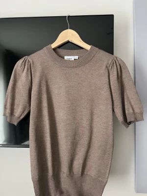 brun stickad tshirt - Snygg beige topp från Saint Tropez med korta puffärmar och rund halsringning. Toppen har ribbade muddar vid ärmslut och nederkant, vilket ger en stilren och modern look. Perfekt att styla med jeans eller kjol. Pris går att diskutera!