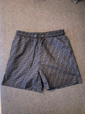 Fendi shorts - Snygga grå shorts från Fendi med det klassiska FF-logomönstret över hela tyget. Shortsen har elastisk midja med snörning och är perfekta för en trendig och avslappnad look. Materialet känns lätt och bekvämt.