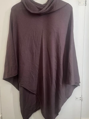 Lila poncho med polokrage - Säljer en oversized lila poncho med polokrage. Ponchon har en lös och flowy passform med asymmetrisk nederkant. Perfekt att slänga över en tröja för extra värme. Materialet känns mjukt och bekvämt.
