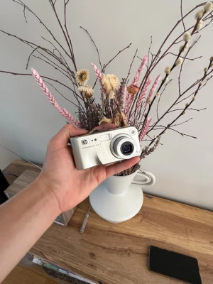 HP Photosmart M417 digitalkamera - Snygg silverfärgad digitalkamera från HP, modell Photosmart M417. Kompakt design med rundade kanter och tydliga knappar. Kameran har en LCD-skärm på baksidan och är tillverkad i plast och metall.