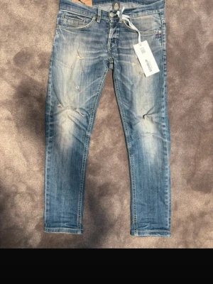 Blå slitna jeans från Dondup - Snygga blå jeans från dondup med slitningar och ljusa tvättade partier. Modellen har klassisk femficksdesign, dragkedja och knapp, samt detaljerade bakfickor. Perfekta för en trendig och avslappnad stil. Tagg medföljer ej!!                    Sitter som 28-29w
