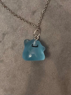 Självlysande Ditto halsband Pokémon smycke Shiny Ditto - Så gulligt halsband med en berlock av en shiny Ditto!Berlocken är ca 1,5 x 1,5 cm och trädd på en kedja i silverimitation, justerbar 40-45 cm. Betlocken är också självlysande och lyser i mörkret.