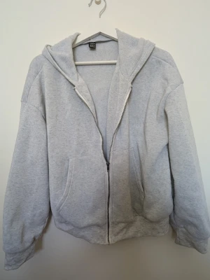 Ljusgrå zip up hoodie - Ljusgrå zip up hoodie. Den har dragkedja framtill, två stora fickor och en klassisk huva. Tillverkad i mjukt sweatshirtmaterial som känns skönt och varmt mot huden. Perfekt för en chill och avslappnad stil. Har använt den några gånger så den är lite nopprig men annars är den i ett bra skick. Skriv gärna om ni har några frågor 💕