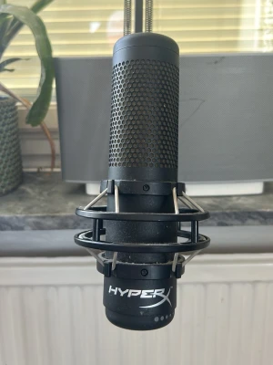 HyperX mikrofon med arm - Säljer en svart HyperX mikrofon med robust metallarm och shock mount. Mikrofonen har ett stilrent, cylinderformat utseende med metallgaller och HyperX-logga. Perfekt för streaming, gaming eller podd. Enkel att montera på skrivbordet. Hittar Tyvär inte orginal stativet skulle kunna leta mer om det önskas, köpte denna arm för 400kr ungefär