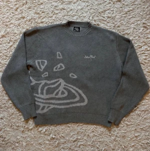 Grå stickad tröja- Broken Planet - Säljer en grå stickad tröja från Stolen Planet med ett unikt abstrakt mönster i ljusgrått på framsidan. Tröjan har rund halsringning, ribbade muddar och är tillverkad i mjukt material. Perfekt för dig som gillar streetwear och snygga detaljer.