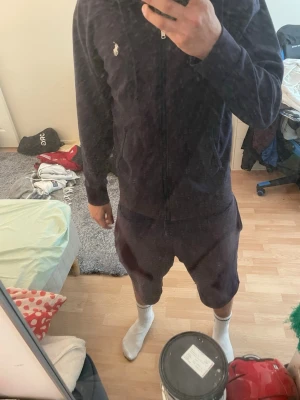 Mörkblå hoodie från Polo Ralph Lauren - Säljer en mörkblå hoodie från Polo Ralph Lauren med dragkedja framtill och klassisk vit logga på bröstet. Hoodien har huva med dragsko och två fickor framtill. Perfekt för en chill och stilren look.