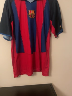 Barcelona Larsson 17 matchtröja - Klassisk Barcelona fotbollströja i rött och blått med klubbmärke på bröstet och Larsson 17 tryckt i gult på ryggen. Tröjan har korta ärmar och krage, perfekt för dig som älskar fotboll och vill visa ditt stöd för laget.