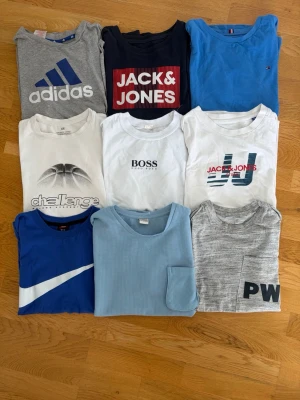 9-pack t-shirts från Adidas, Nike, Boss m.fl. - Säljer ett paket med 9 t-shirts i olika färger och stilar från Adidas, Nike, Boss, Jack & Jones och H&M. Färgerna är blå, vit, grå och svart. Några har tryck och loggor, vissa är enfärgade. Perfekt för dig som vill ha variation i garderoben.
