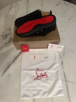 Svarta sneakers från Christian Louboutin - Snygga svarta sneakers från Christian Louboutin med ikonisk röd sula och svarta skosnören. Skorna har en låg profil och är tillverkade i mocka med läderdetaljer. Perfekta för dig som vill ha en exklusiv och trendig look.