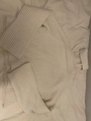 Vit ribbstickad polotröja - Säljer en vit ribbstickad polotröja med hög krage och långa ärmar. Tröjan har en oversized passform och är gjord i ett mjukt, tjockt material som passar perfekt för kyliga dagar. Enkel och stilren design som är lätt att matcha.