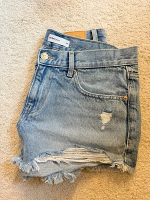 Ljusblå denimshorts  - Snygga ljusblå denimshorts från Gina Tricot med fransig och riven kant, slitningar framtill och klassisk femficksdesign. Perfekta för sommaren och ger en avslappnad vibe till din outfit.