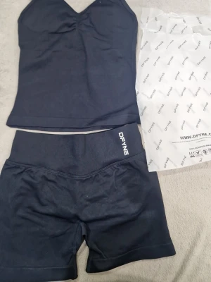 Svart set från DFYNE med topp och shorts - Snyggt svart underklädesset från DFYNE med en tight topp med smala axelband och matchande shorts. Setet är gjort i stretchigt material, 90% nylon och 10% elastan, vilket ger en bekväm och följsam passform. Perfekt för dig som gillar stilrena och sportiga underkläder.