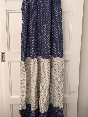 Blommig långklänning Gerard Darel - Långklänning från Gerard Darel i blått och vitt med små blommor. Klänningen har knytband upptill och ett luftigt, flowy fall. Perfekt för sommarens varma dagar och har en bohemisk vibe.