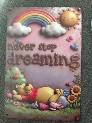 Metallskylt Nalle Puh Never Stop Dreaming - Säljer en söt metallskylt med motiv av Nalle Puh och Nasse som ligger i gräset under en regnbåge och sol. Texten 'never stop dreaming' står i relief. Skylten har färgglada detaljer med blommor, fåglar och moln. Perfekt som dekoration i sovrum eller barnrum.
