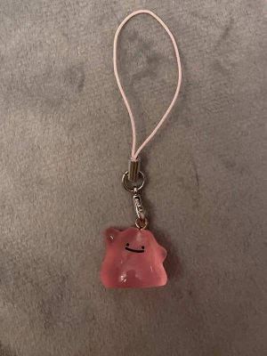 Ditto Mobilsmycke Pokemon hänge Ditto Nyckelring Pokemon   - Jättegulligt hänge med en ljust rosa Ditto! Den är dessutom självlysande och lyser i mörkret.   Ditto-berlocken är ca 1,5 x 1,5 centimeter. Öglan är ca 5 cm lång.  Jättefin att sätta på din mobil, väskan, ditt 3DS, Switch eller i nycklarna exempelvis! 