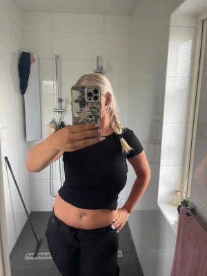 Svart croppad topp med öppen rygg - Snygg svart croppad topp med korta ärmar och öppen rygg som knyts baktill. Perfekt för dig som vill ha en trendig och stilren look. Toppen har en tight passform och är tillverkad i ett stretchigt material.