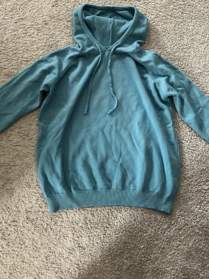 Blå Kashmir Hoodie  - Snygg blå hoodie med huva. Tillverkad i mjukt Kashmir som känns skönt mot huden. Klassisk passform med ribbade muddar vid ärmslut och nederkant. Perfekt för en avslappnad och chill stil. Funkar utmärkt till både tjejer och killar och är aldrig använd. 