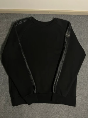 Colmar – Black Sweatshirt (L) - Elegant and minimalist Colmar sweatshirt in deep black. Size L, length 68 cm, width 56 cm – offering a relaxed yet refined fit. The sleeve features the signature Colmar logo badge, adding a subtle touch of sophistication to the clean design.  ✅ Condition: Excellent – no stains, no damage 💯 Authenticity: 100% genuine Colmar product 🧵 Material: Warm, premium-quality fabric with smooth satin-like detailing – durable, soft, and comfortable 📦 Shipping: Sent immediately after purchase