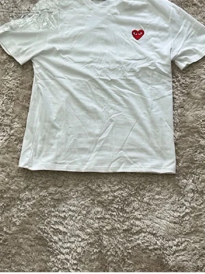 Vit Comme des Garçons Play t-shirt - Vit t-shirt från Comme des Garçons Play med det ikoniska röda hjärtat med ögon broderat på bröstet. Klassisk passform och rund halsringning. Perfekt basic med en twist för dig som gillar streetwear vibes.