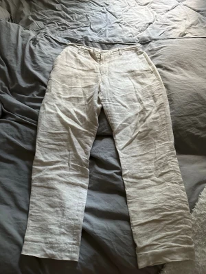 Beiga linnebyxor - Snygga och luftiga linnebyxor i beige med raka ben och klassisk passform. Byxorna har hällor för skärp, fickor fram samt elastisk midja baktill för extra komfort. Perfekta för en avslappnad och stilren look.