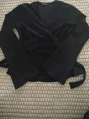 Svart omlottopp från Missay - Svart omlottopp från Missay med långa ärmar och knytband i midjan. Toppen har en v-ringad design och är figurnära med en stilren look. Perfekt för dig som gillar enkla men snygga plagg.