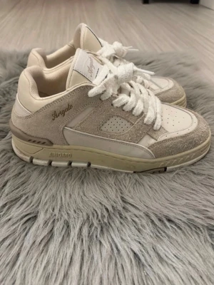 Beige sneakers från Axel Arigato - Snygga beige sneakers från Axel Arigato med ovandel i mocka och läder. Skorna har vita snören, perforerade detaljer på tån och sidan samt diskret logga i guld på sidan. Tjock sula i beige ton ger en trendig look. Perfekta för dig som gillar stilrena och moderna sneakers. ⚠️SKORNA RENGÖRS INNAN DEN SKICKAS