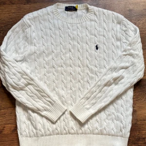 Vit kabelstickad sweatshirt Polo Ralph Lauren - (L men passar som M, skickar samma dag✅) Kabelstickad vit tröja från Polo Ralph Lauren med klassisk rund halsringning och marinblå broderad logga på bröstet. Tröjan har ribbade muddar vid ärmslut och nederkant och är tillverkad i mjukt material som känns lyxigt och bekvämt. 