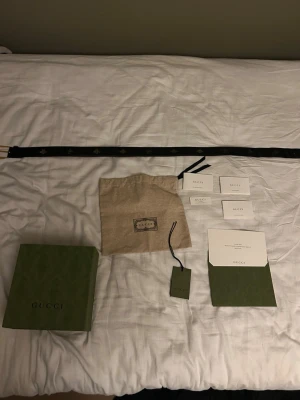 Svart skärp med bi-detaljer från Gucci - Snyggt svart skärp från Gucci i skinn med guldfärgat spänne och ikoniska bi-detaljer längs hela bältet. originalförpackning, dustbag och äkthetskort finns men medföljer tyvärr inte. Bältet är köpt på nk för ungefär 2 år sedan men har tyvärr tappat bort kvittot och bältet kommer inte till användning längre så det är en perfekt accessoar för att lyfta din outfit.