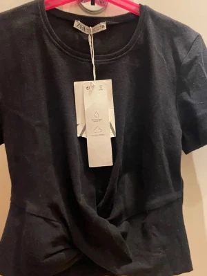 Svart twistad topp från Zara - Snygg svart topp från Zara med twistad detalj framtill. Croppad tröja. Aldrig använd pga för liten.
