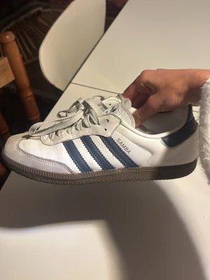 Adidas Samba vita och blå sneakers - Klassiska Adidas Samba sneakers i vitt läder med mörkblå detaljer. Jätte fina. Andvända men inte söndriga eller något spnt