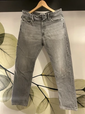 Grå Jack & Jones Chris Relaxed Jeans - Snygga grå jeans från Jack & Jones med rak passform och klassisk femficksdesign. Jeansen har en ljusgrå tvätt och är gjorda i kraftigt bomullstyg. Perfekta för en avslappnad och trendig look.