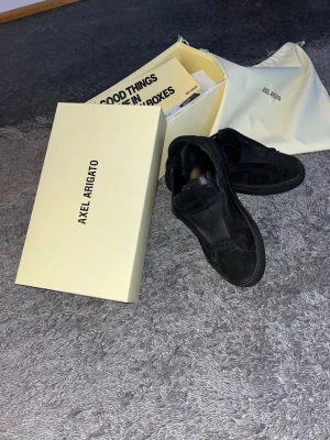 Svarta Axel Arigato sneakers - Säljer ett par svarta sneakers från Axel Arigato i mocka. Klassisk låg modell med stilren design utan snören. De är i storlek 41, jag har tagit bra hand om skorna och borstat dom när det behövts så mockan är fortfarande fin. Skorna kommer med originalkartong och dustbag. Perfekta för dig som gillar minimalistisk och clean stil.