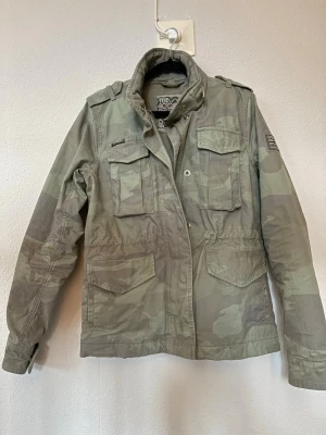 Superdry camo field jacket - Tja , jag säljer nu en riktigt schysst field jacket som är perfket nu när det varmare vädret börjar komma. Den är i storlek 36 vilket passar XS/S. Tveka inte på att skriva om du har några funderingar!! Pris kan absolut diskuteras vid en snabb och smidig affär!